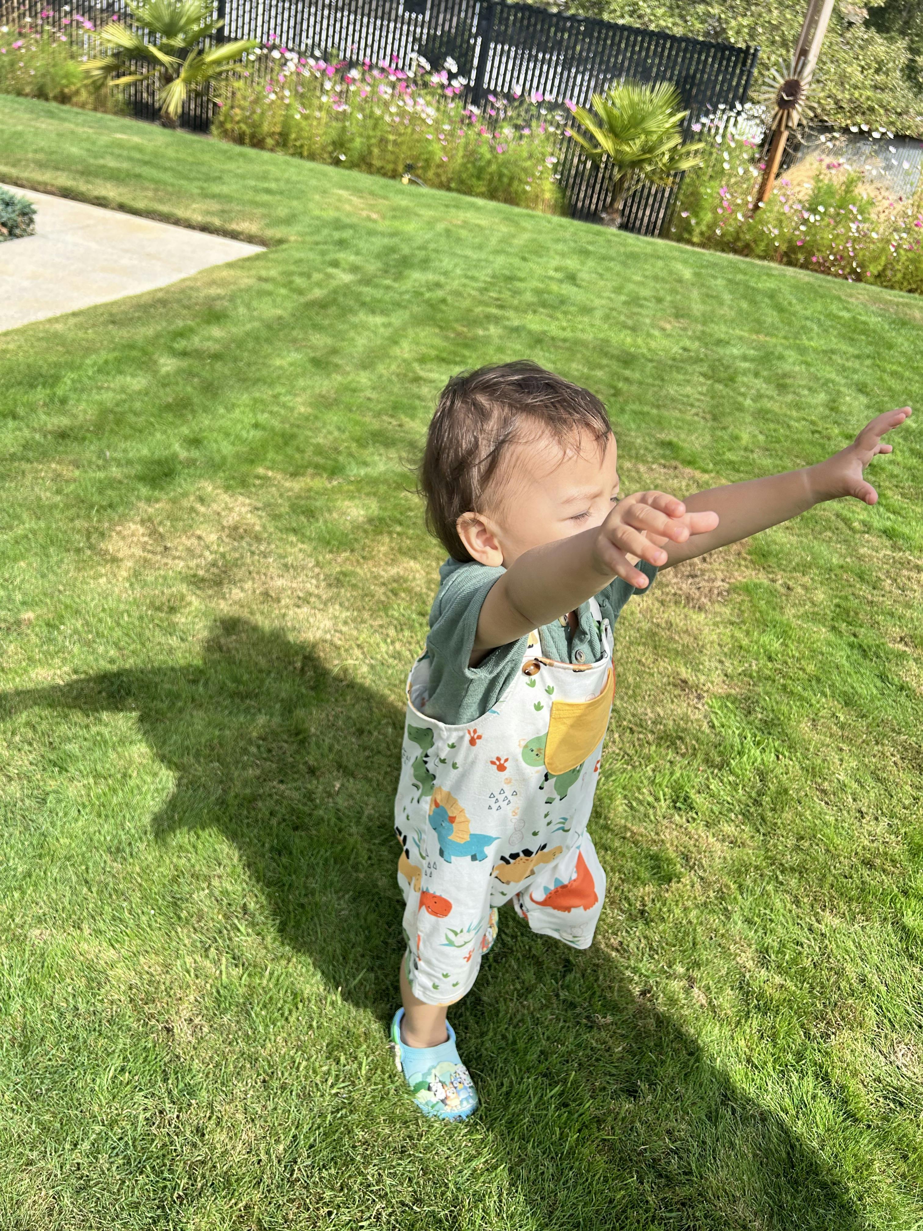 A small child reaching forward while walking on a grassy lawn