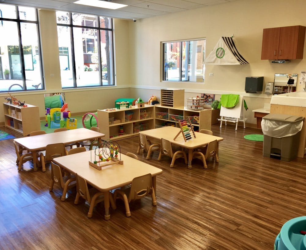 Empty classroom with small tables and chairs, shelves with toys