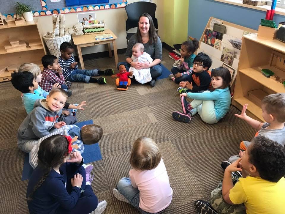 Adult holding an infant surrounded by children sitting on the floor