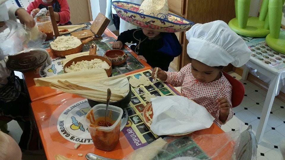 Child in chef hat at a table with food and another child in a sombrero