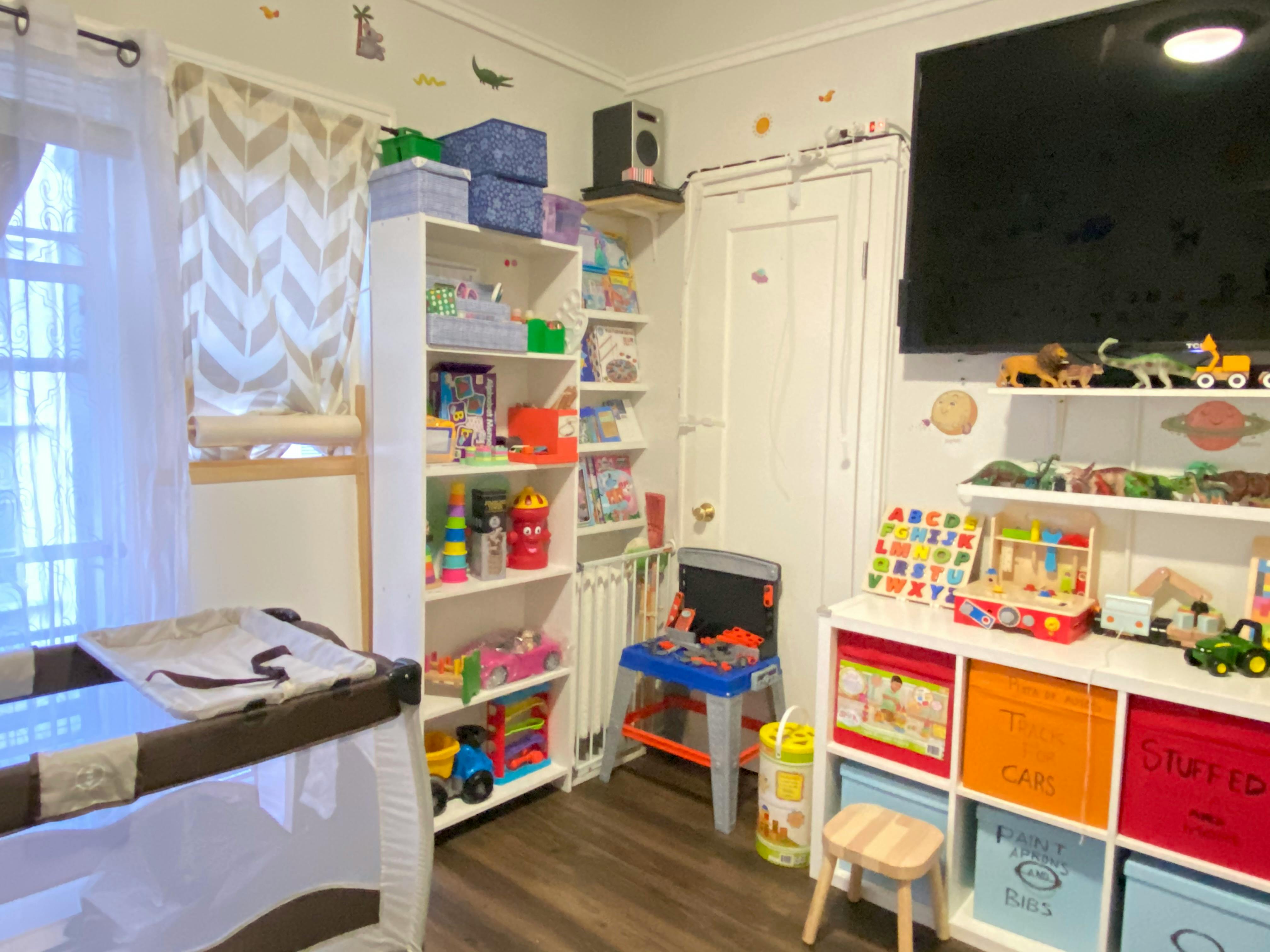 Nursery room with a crib, shelves of toys, and a small play table