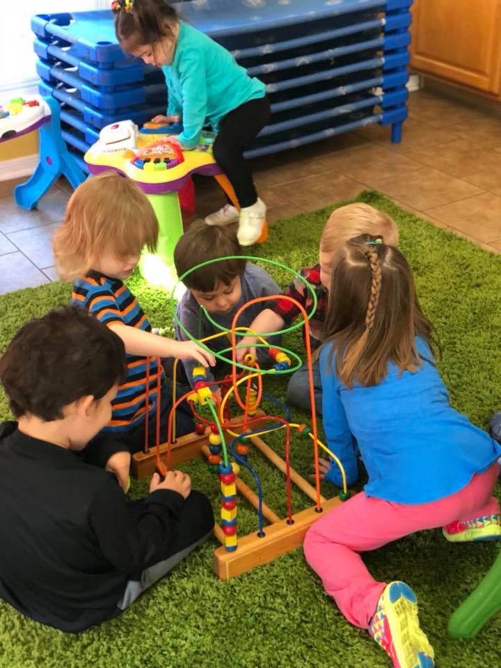 Children playing with a bead maze toy on a green rug