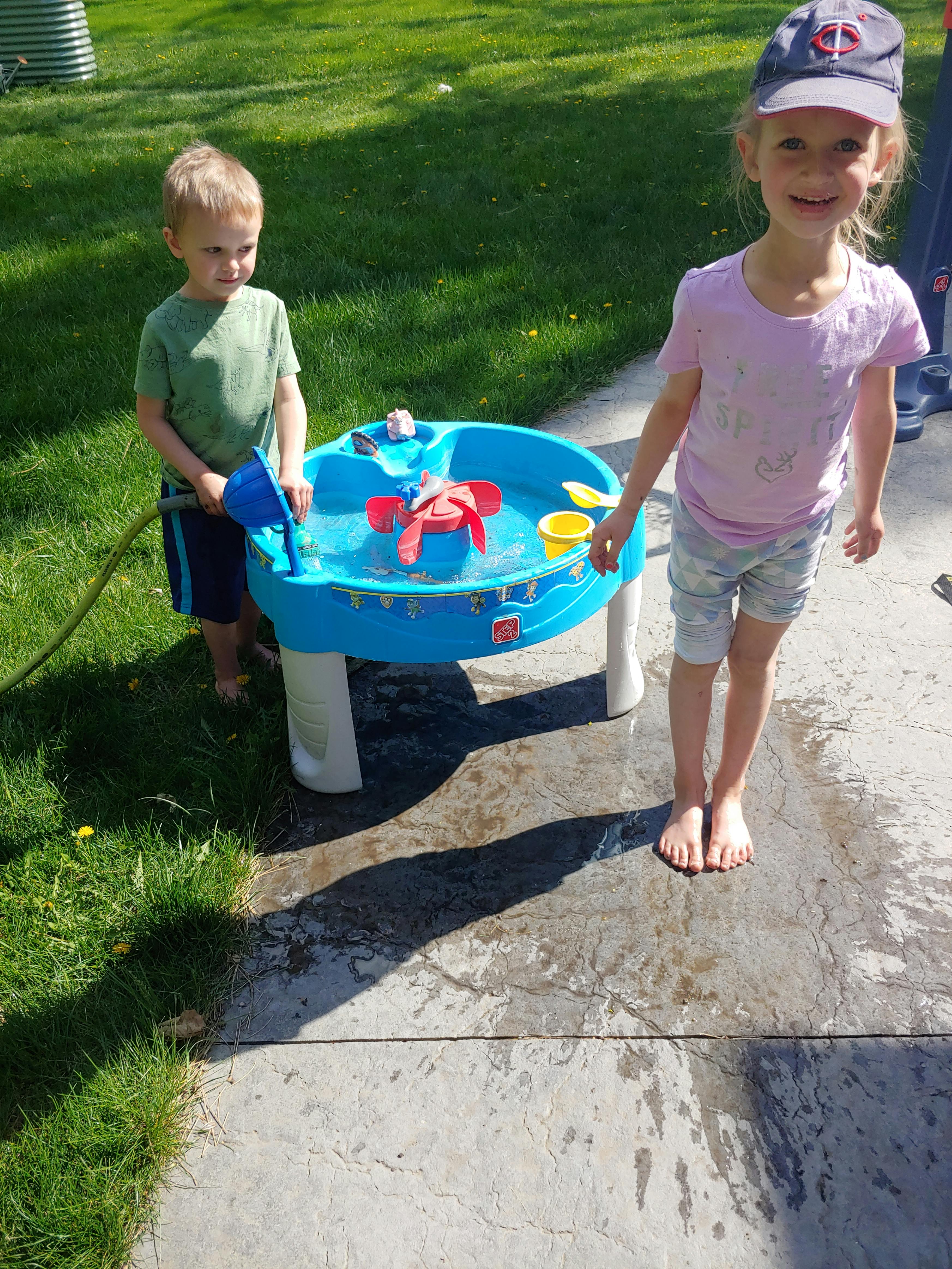 Two children playing with a water table outdoors
