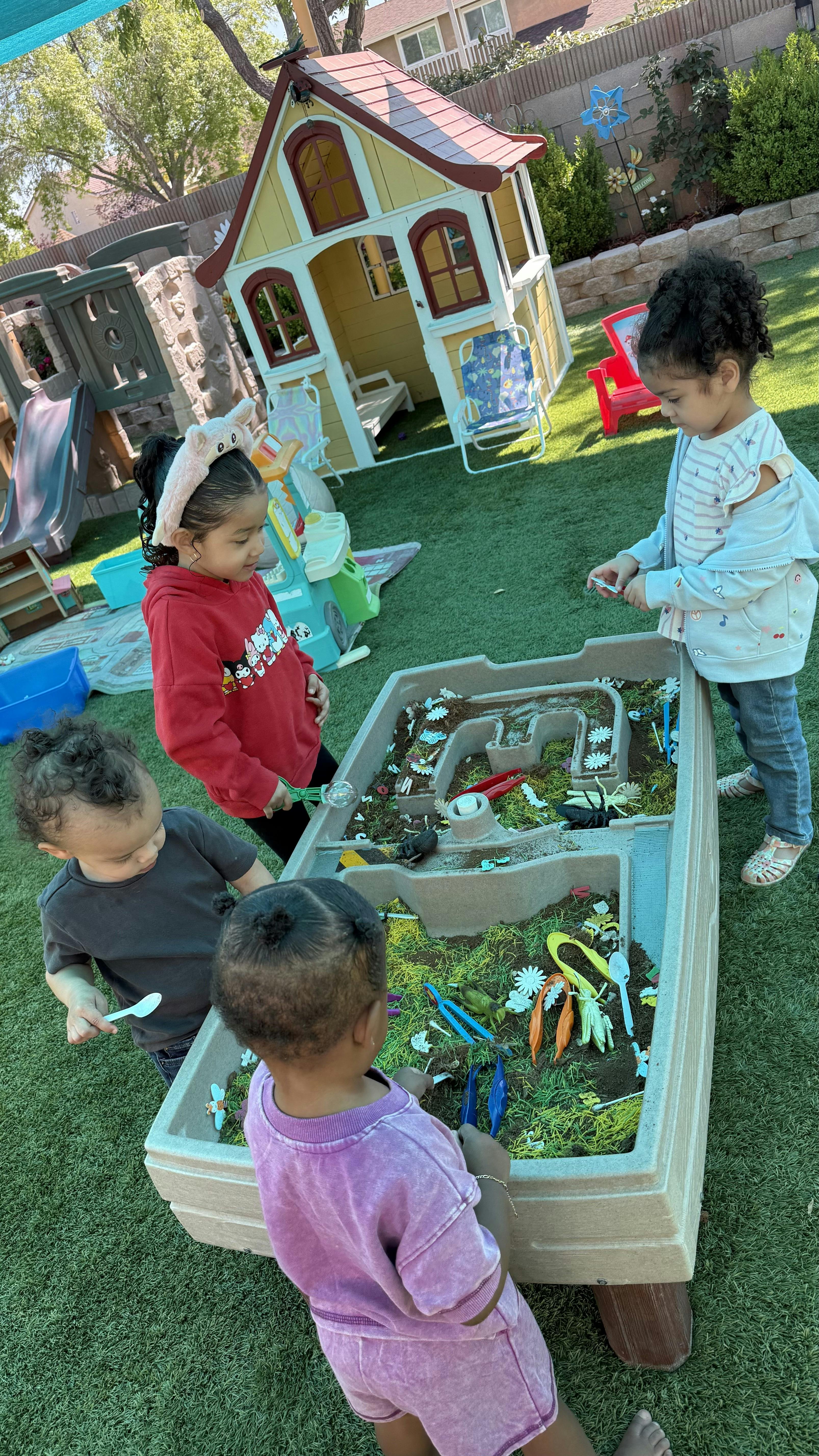 Four children playing around a sensory table with dirt and artificial grass