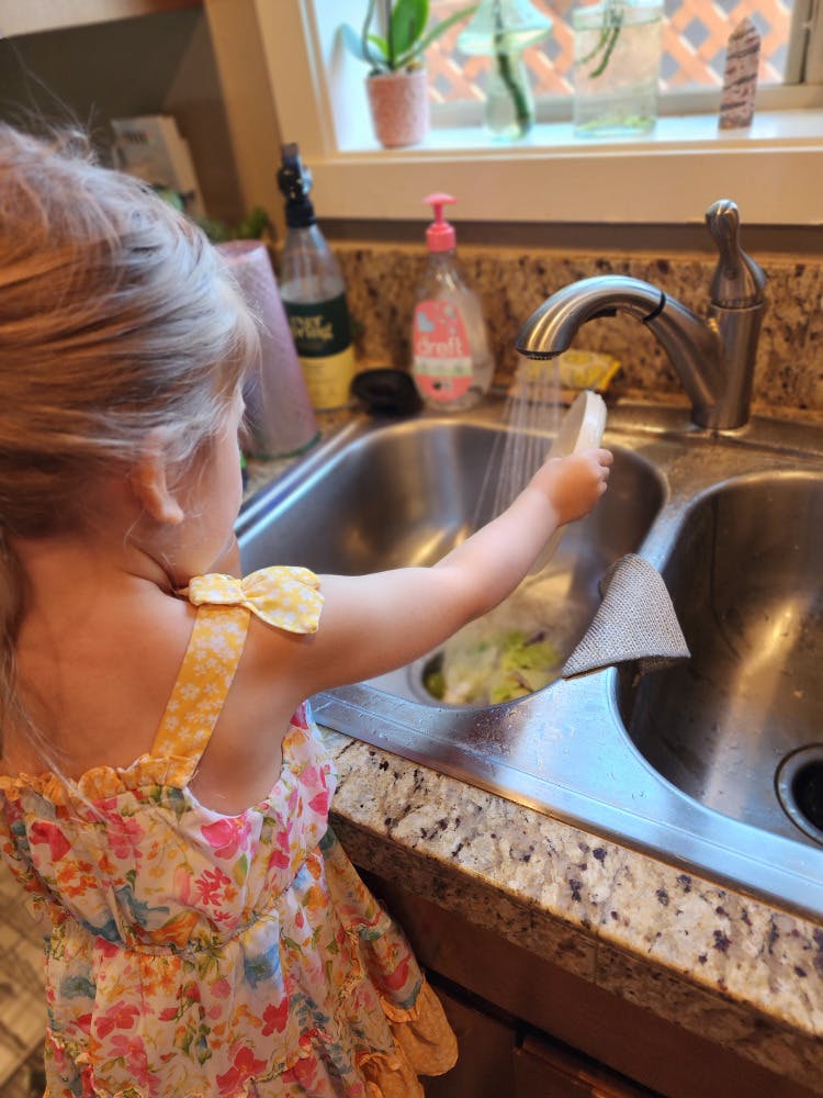 Child washing a plate under a kitchen faucet