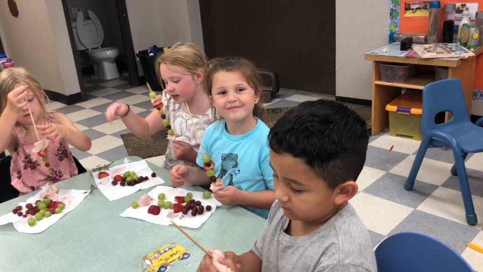 Children making fruit skewers in a classroom