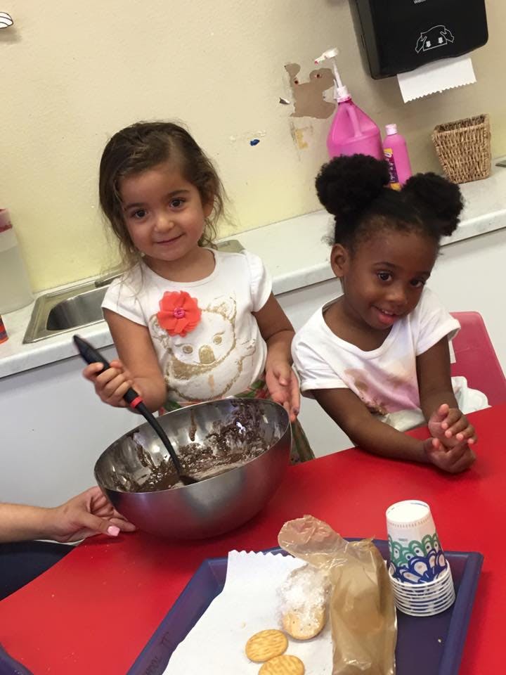 Two children at a table, one stirring a bowl of batter