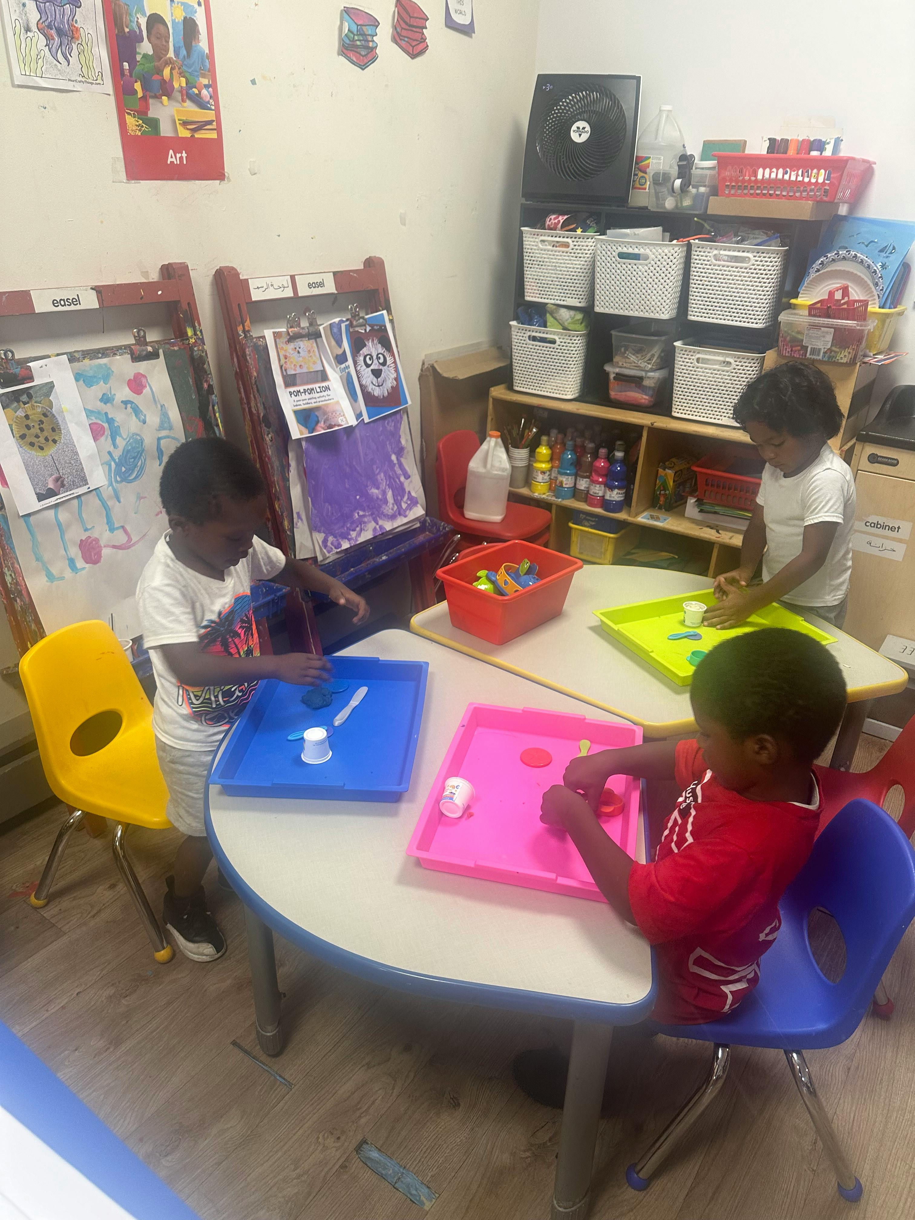 Three children playing with trays at a table in a classroom