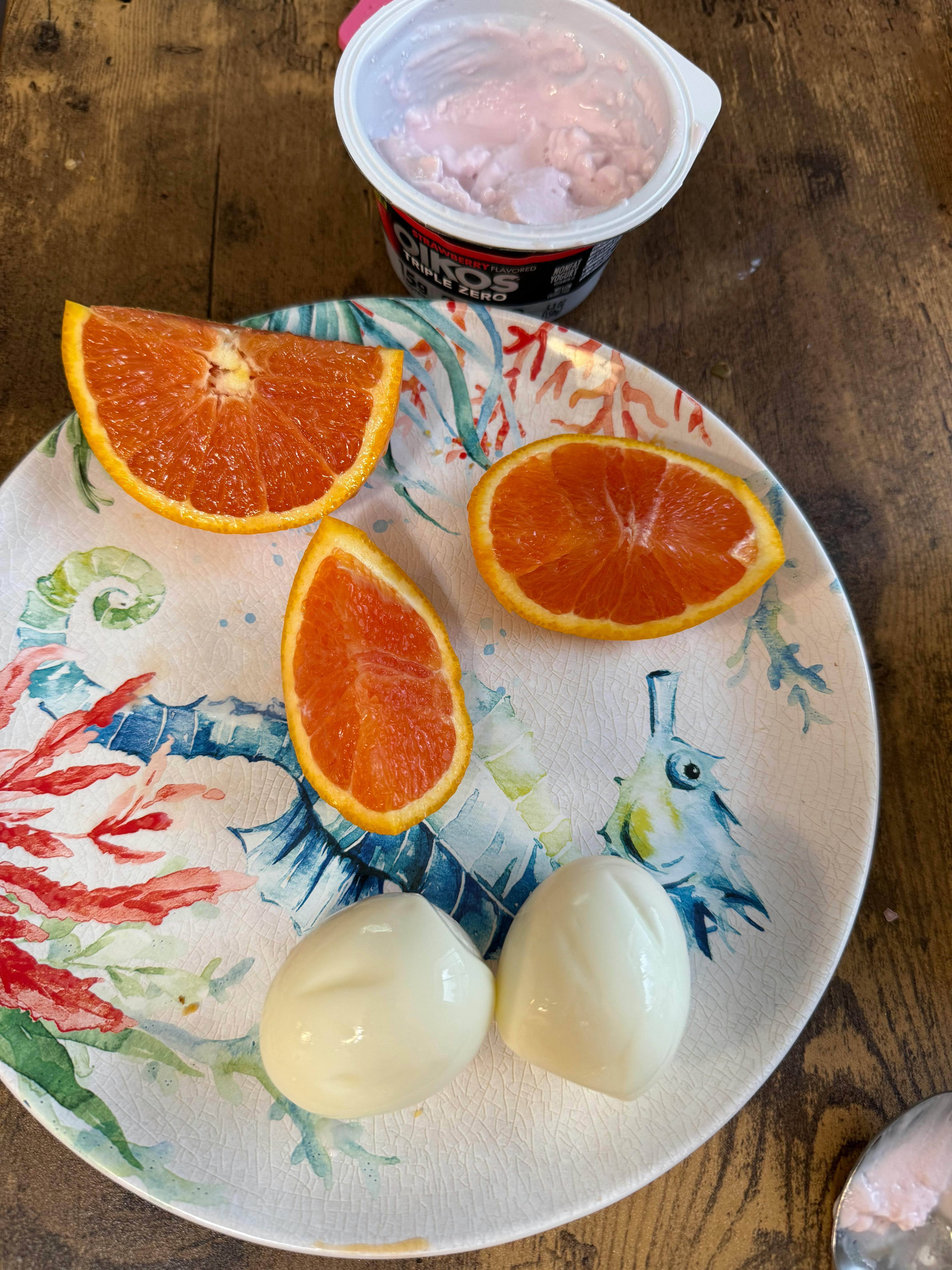 Plate with orange slices and peeled hard-boiled eggs, and a container of yogurt