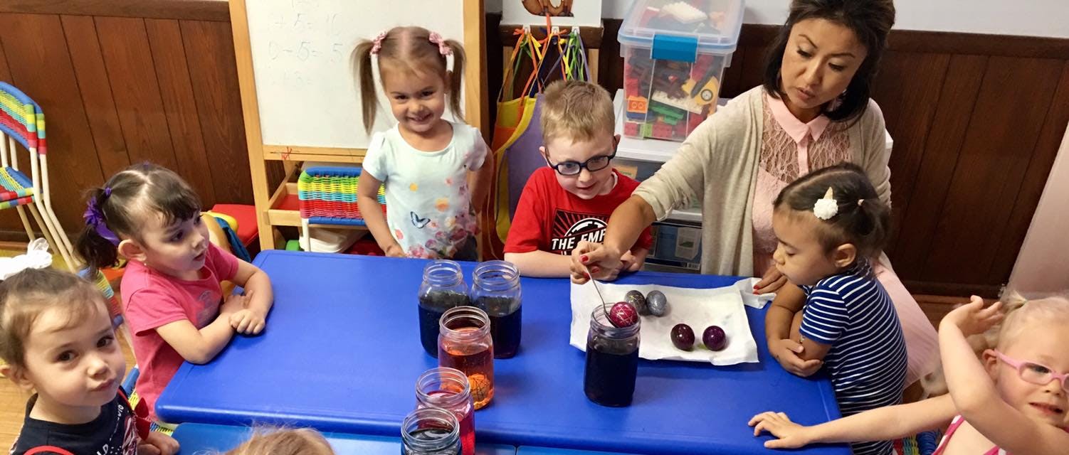 Adult and children at a table with jars and small objects in a classroom