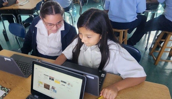 two children in a classroom looking at a laptop screen together