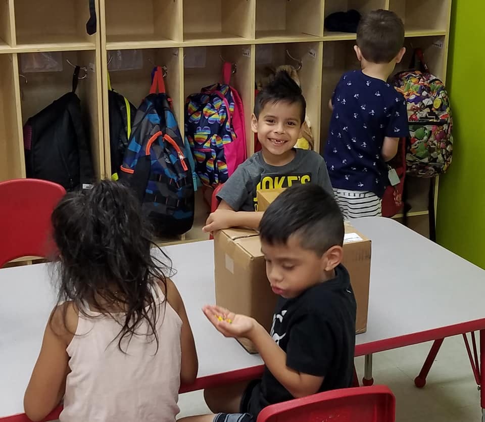 Children at a table with a box, one child holding small objects