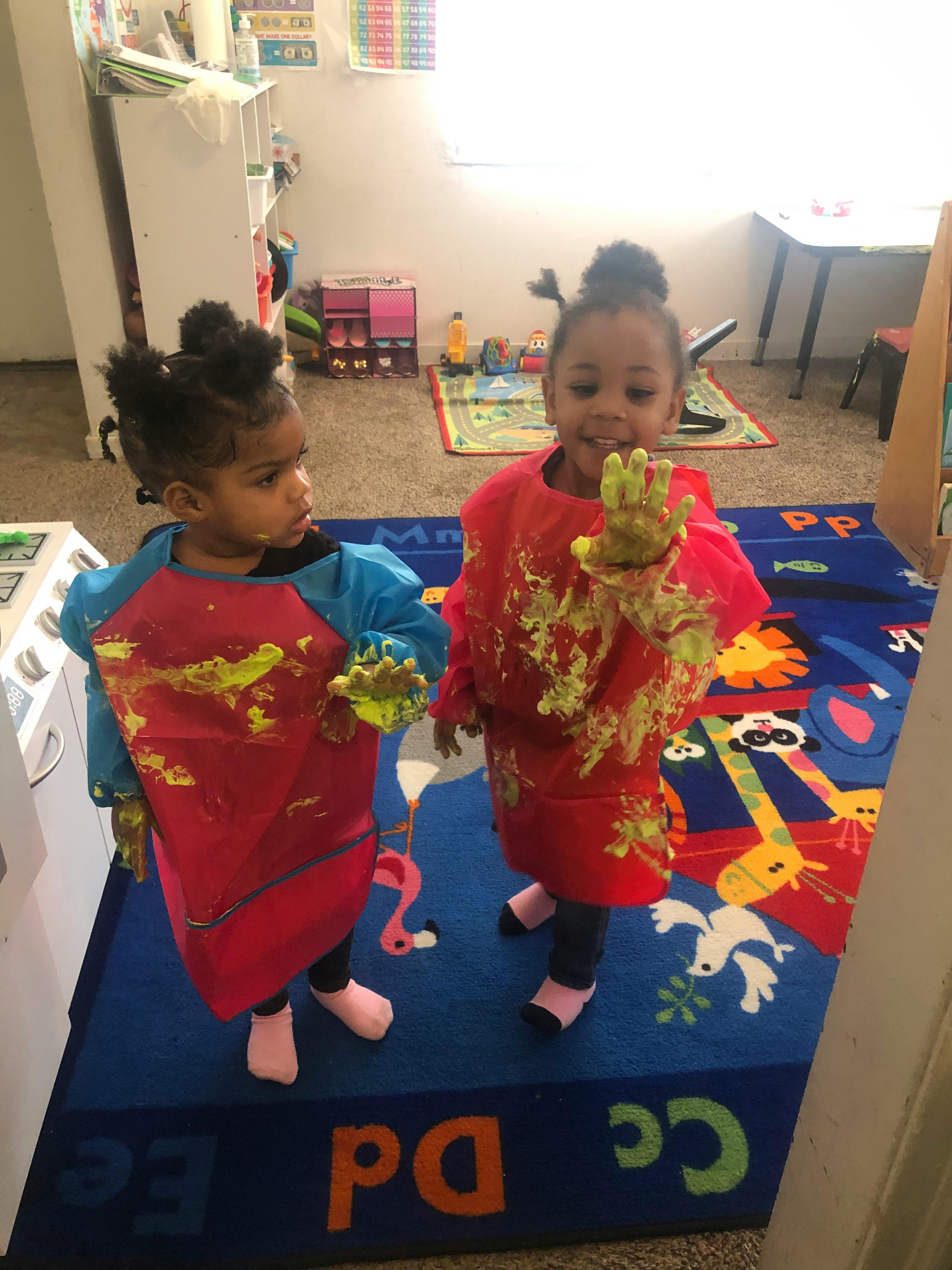 Two children in paint-splattered smocks with paint on their hands