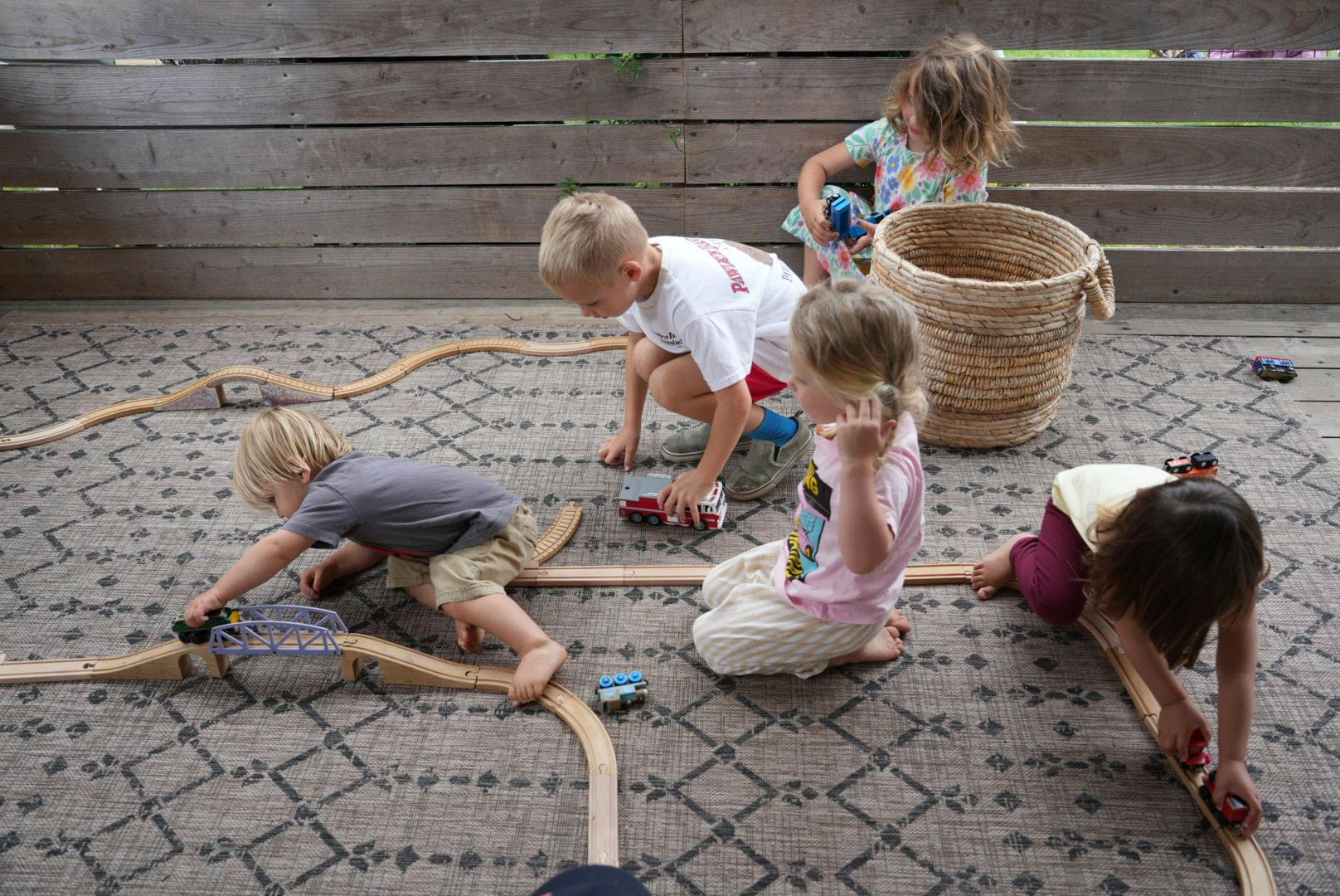 Four children playing with a wooden train set on a rug