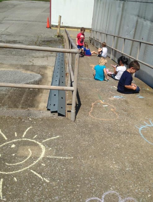 Children sitting on a paved surface with chalk drawings