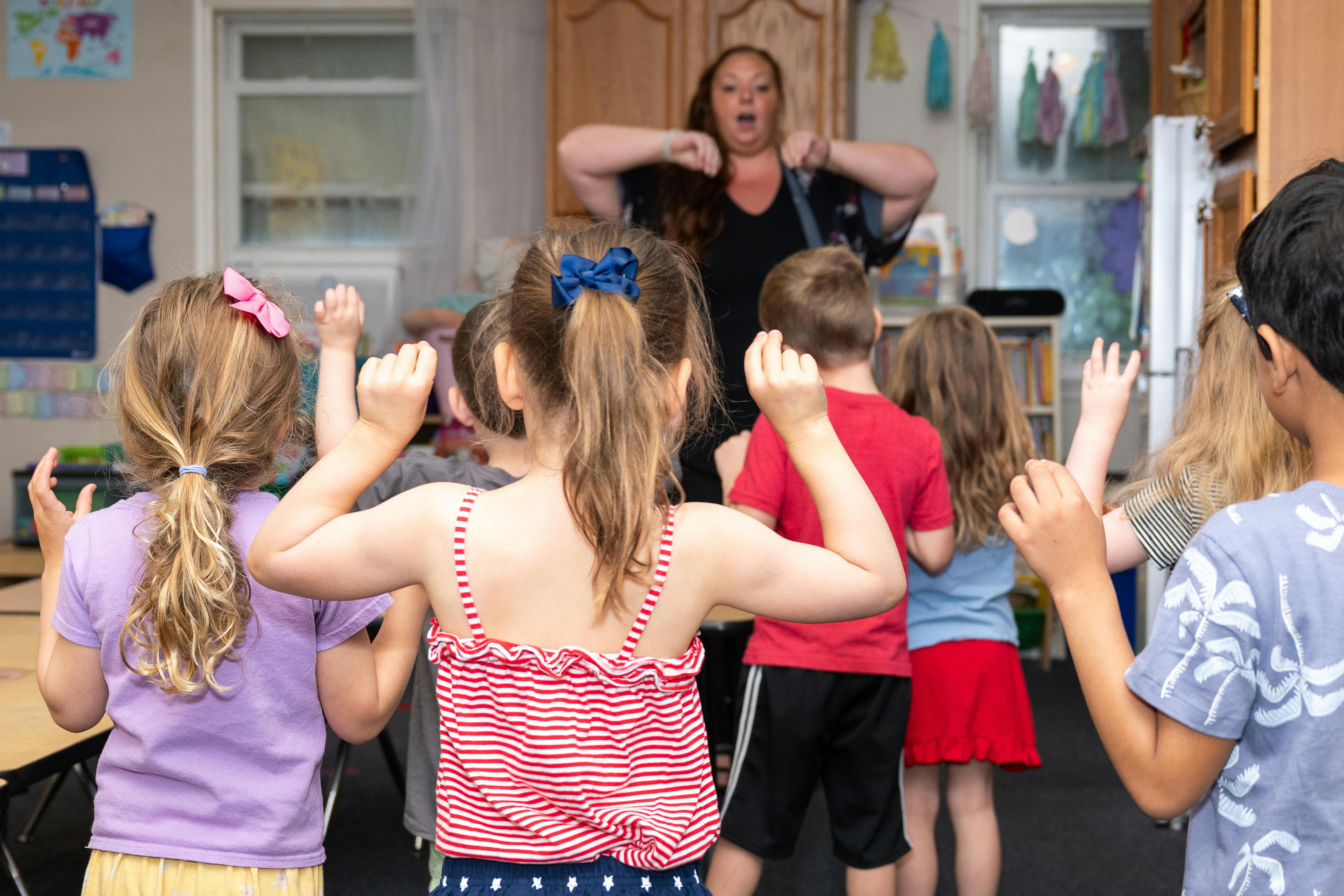 Adult leading a group of children in an activity with raised arms