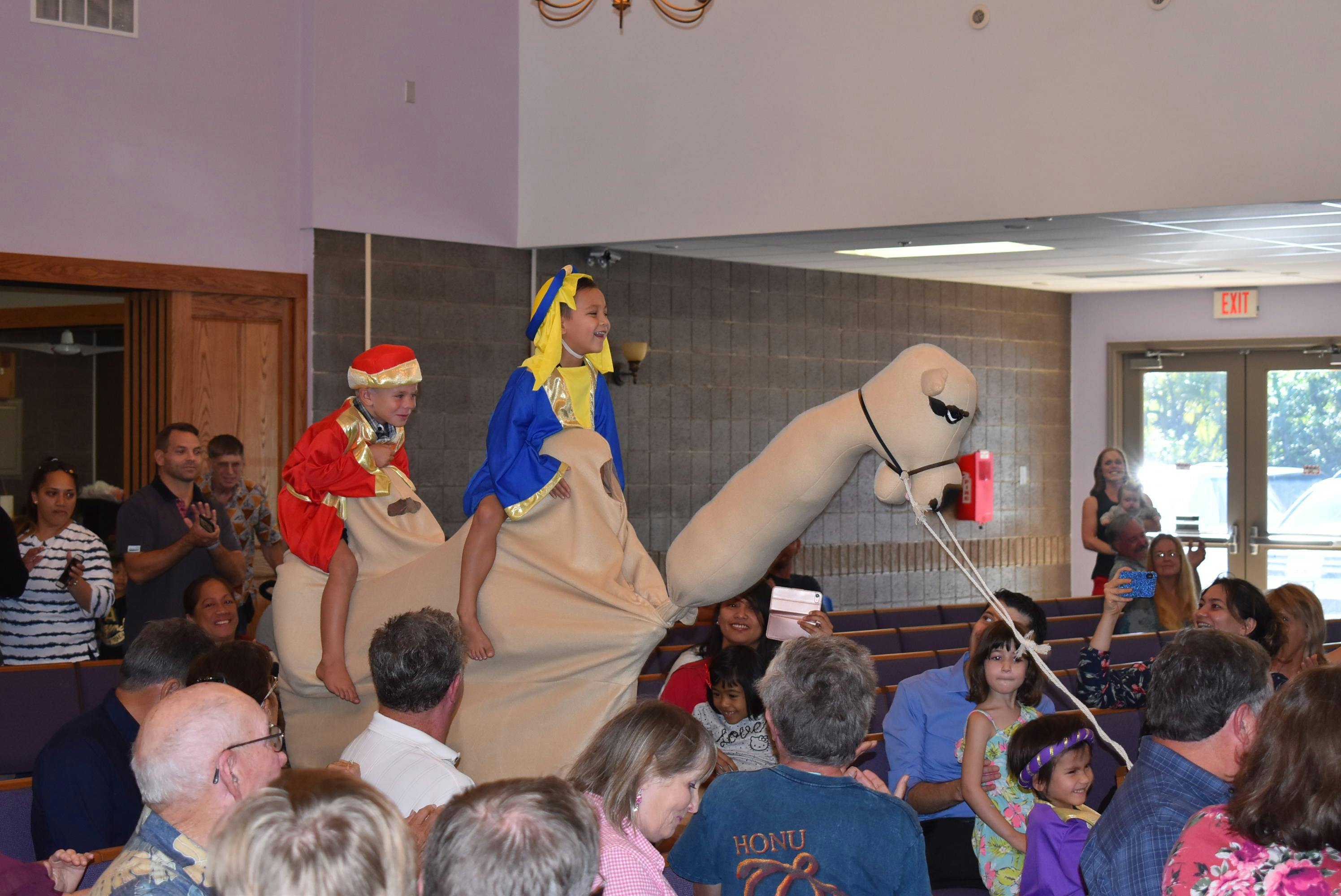 Two children in costumes riding a camel prop in front of an audience
