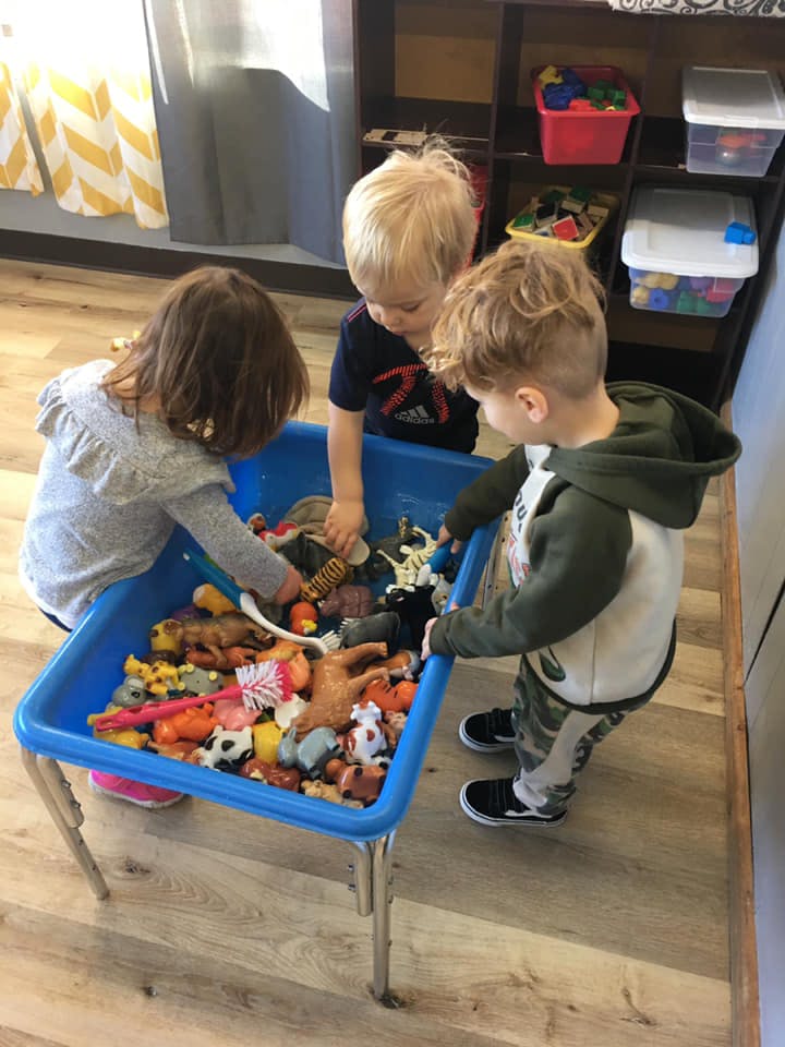 Three children playing with toys in a blue bin