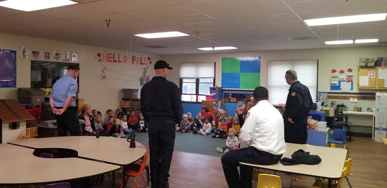 Adults speaking to children sitting on the floor in a classroom