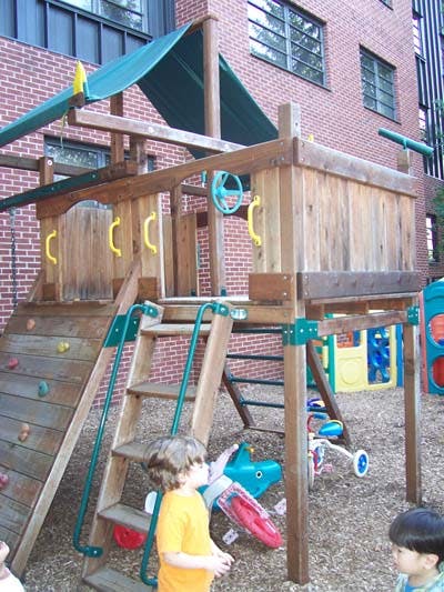 Child standing near a wooden playground structure with a slide and ladder