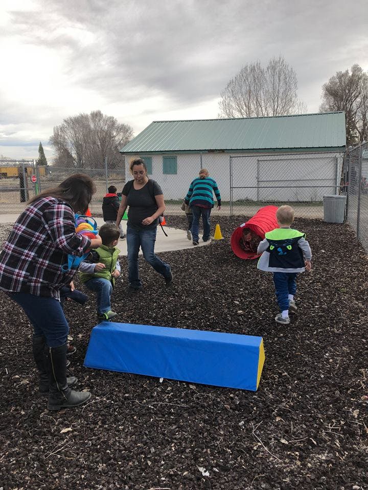 Adults and children playing outdoors with a red tunnel and blue beam