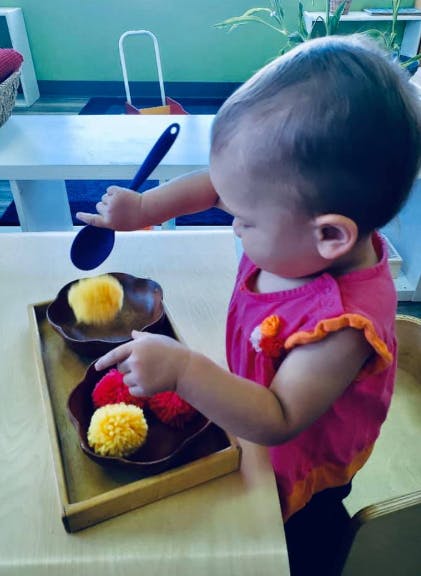 Child playing with pom-poms and a spoon