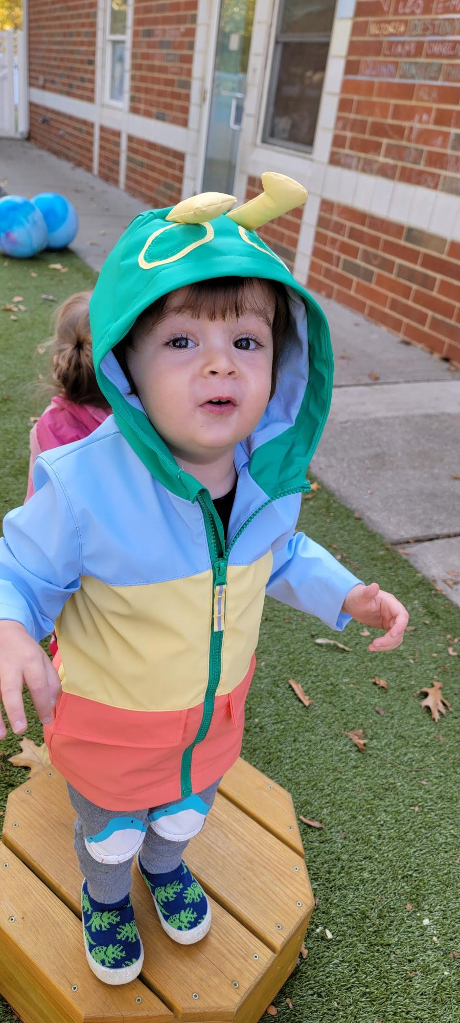 Child in a green caterpillar costume standing on a wooden platform