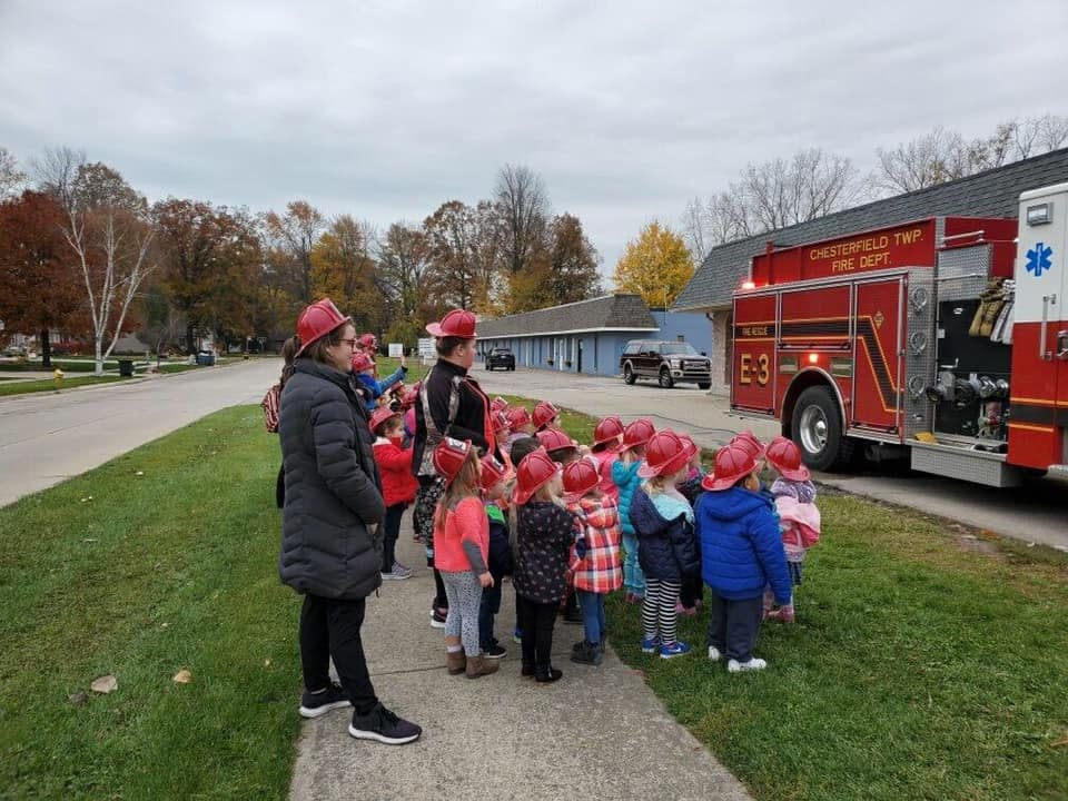 Adults and children in red hats looking at a fire truck