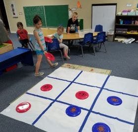 Children playing tic-tac-toe with frisbees on a large mat