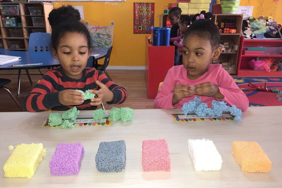 Two children playing with colorful modeling clay at a table in a classroom