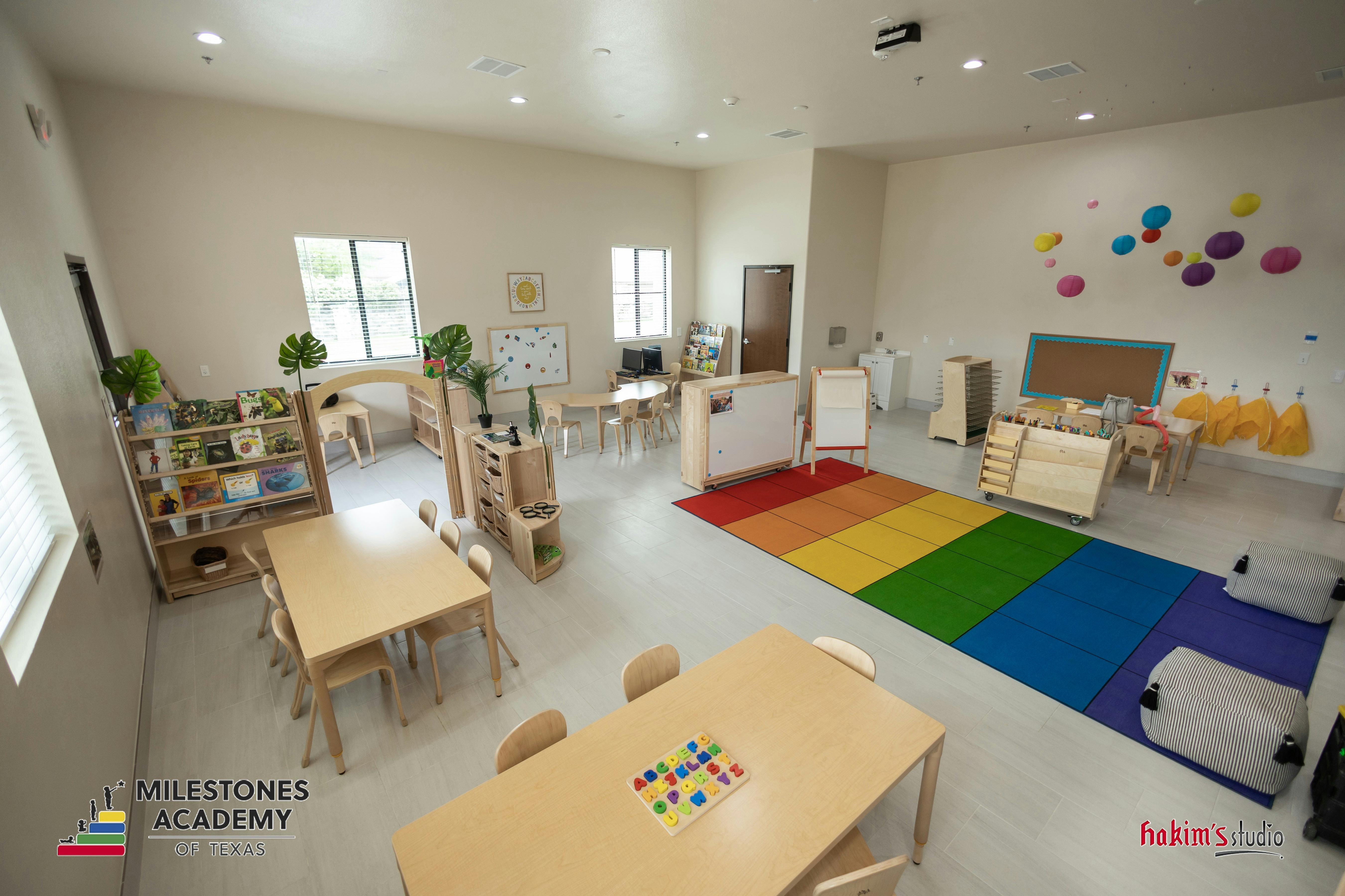 Classroom with child-sized tables, chairs, bookshelves, and a rainbow-colored rug