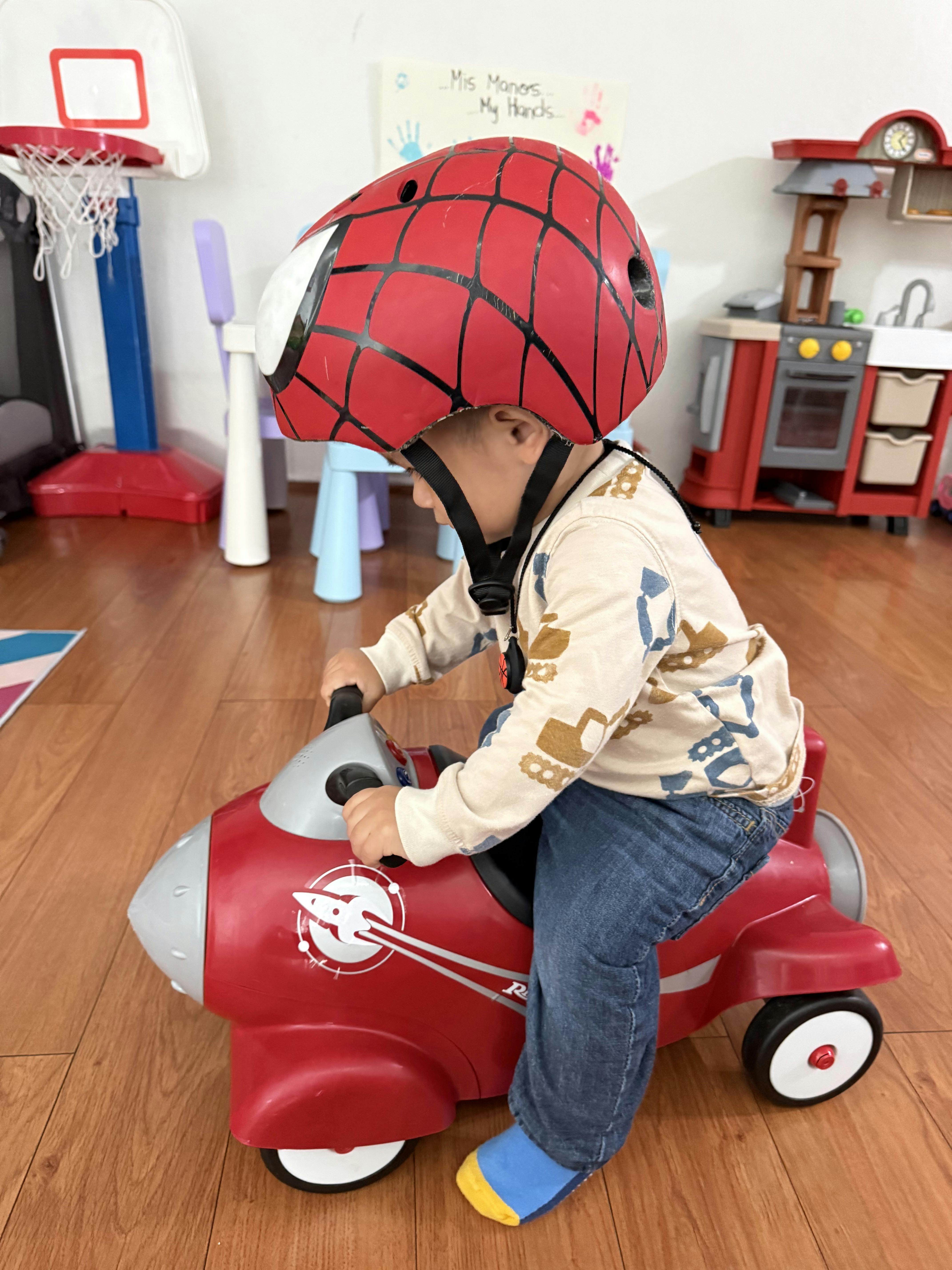 Child in a Spiderman helmet on a red toy plane