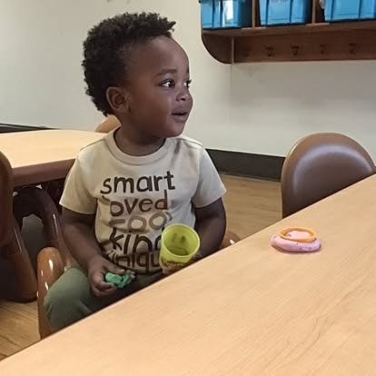 Child sitting at a table with a cup and toy