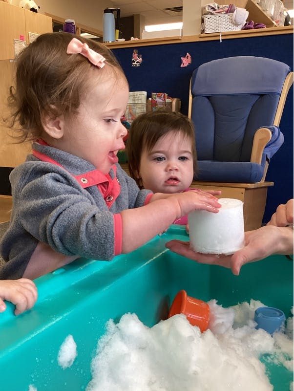 Two children playing with snow in a sensory bin