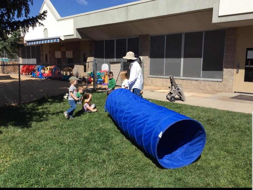 Person and children playing with a blue tunnel on a grassy area