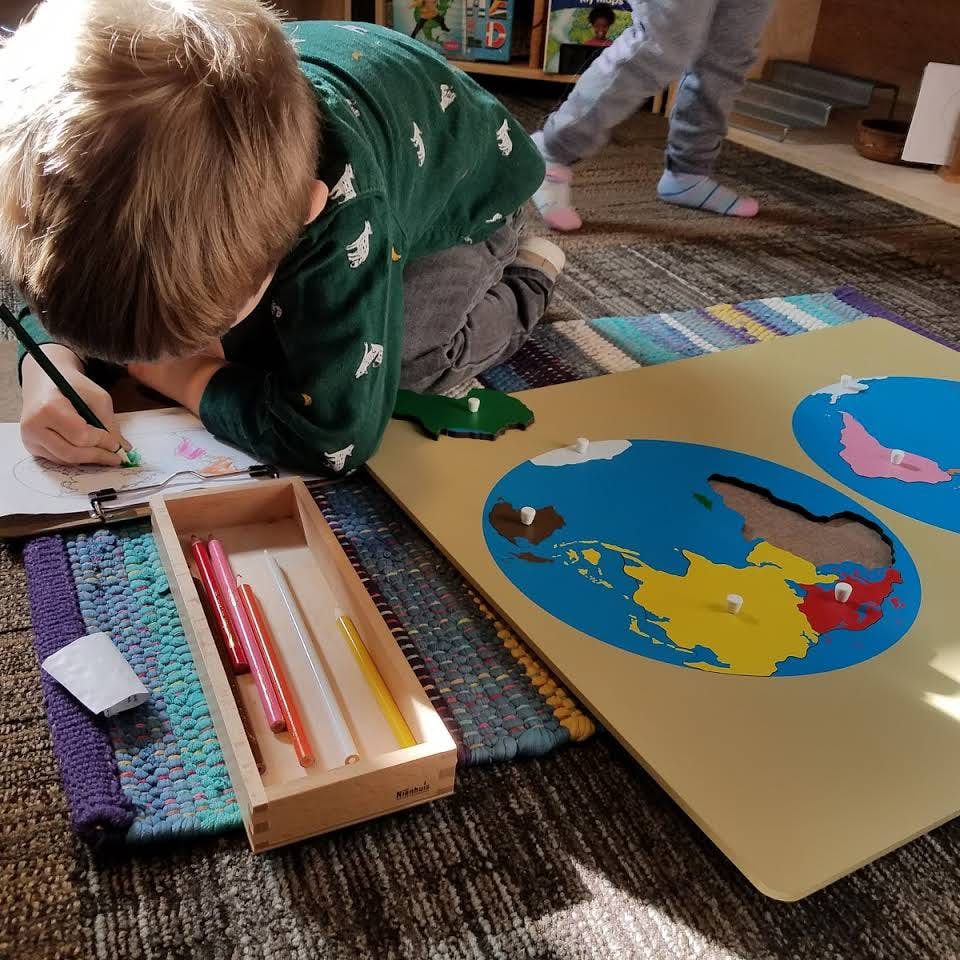 Child drawing on paper next to a world map puzzle