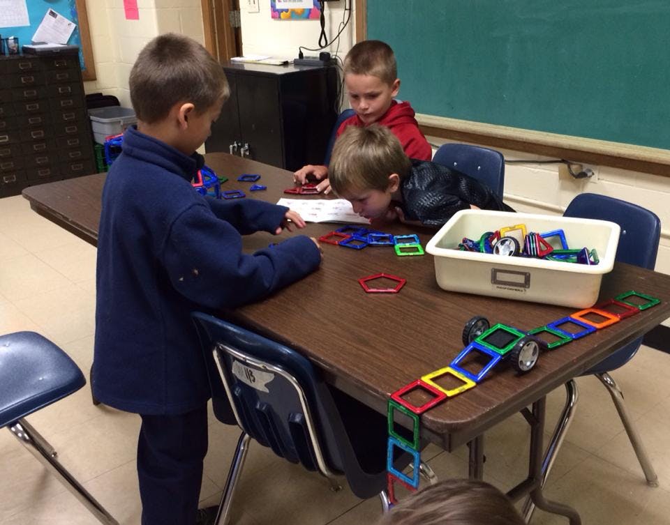 Three children playing with colorful magnetic tiles at a table