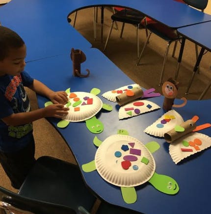 Child making crafts with paper plates and colorful shapes on a blue table