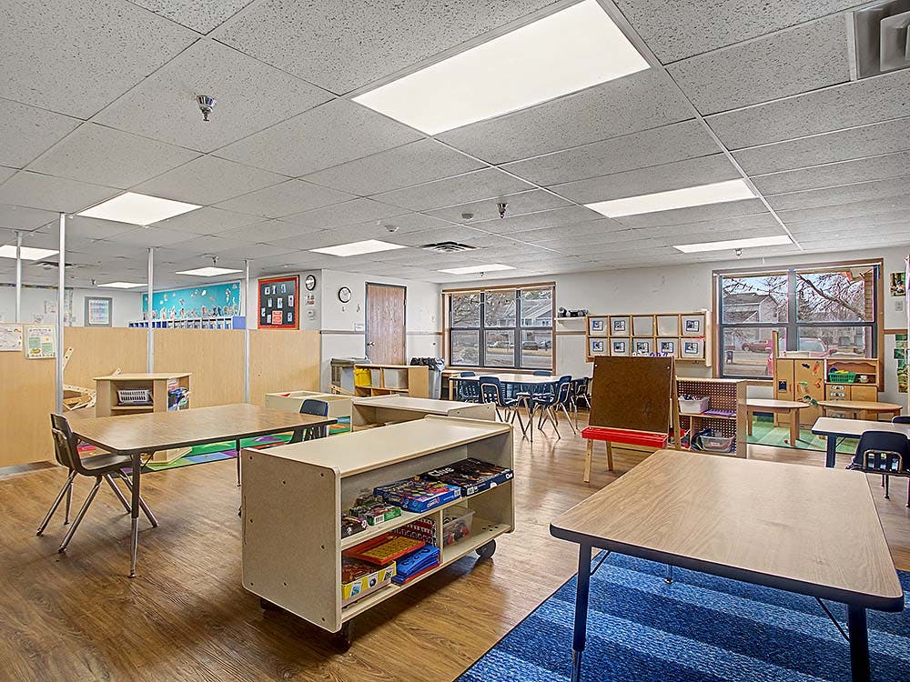 Empty classroom with small tables, chairs, and shelves of toys