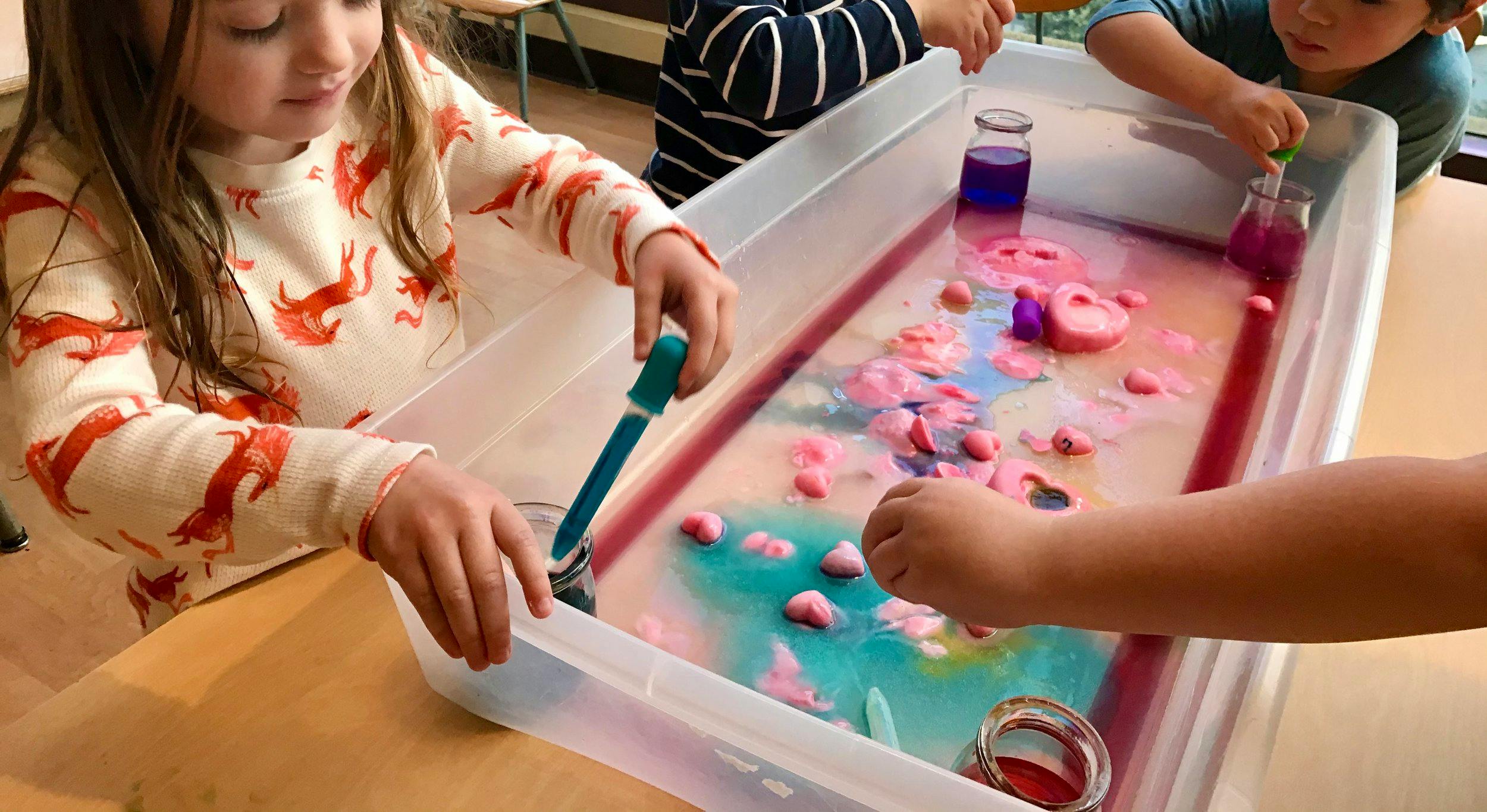 Child using a dropper in a sensory bin with colored water and objects