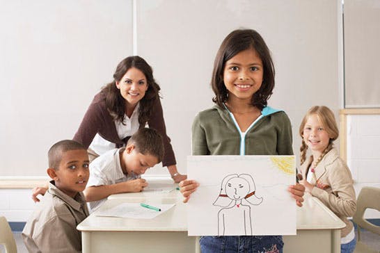 Adult and three children in a classroom, one child holding up a drawing