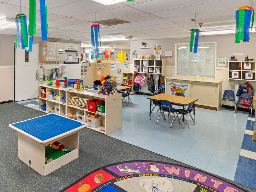 Classroom with tables, chairs, shelving units with toys, and wall decor