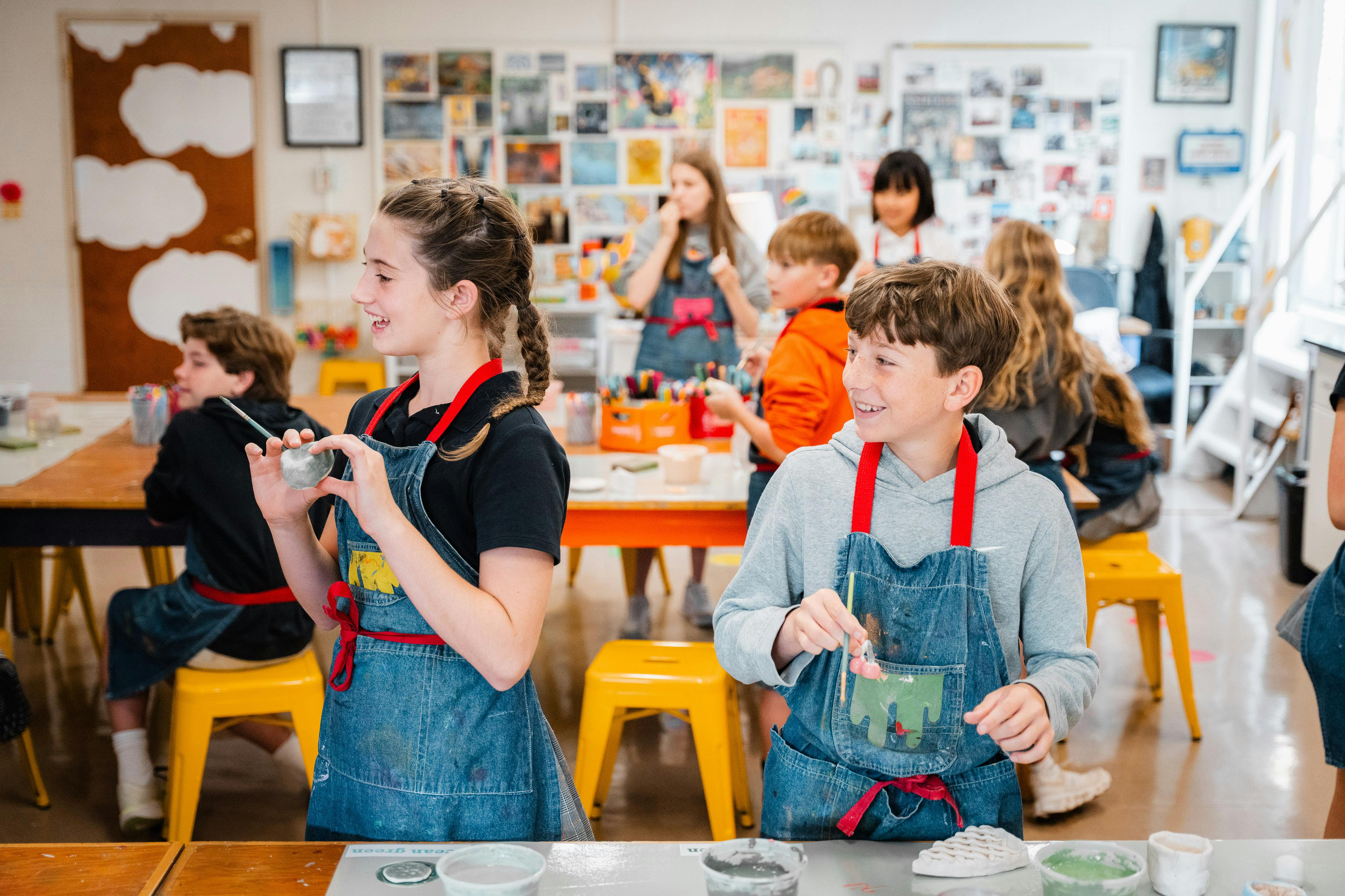 People wearing aprons painting clay objects in a classroom
