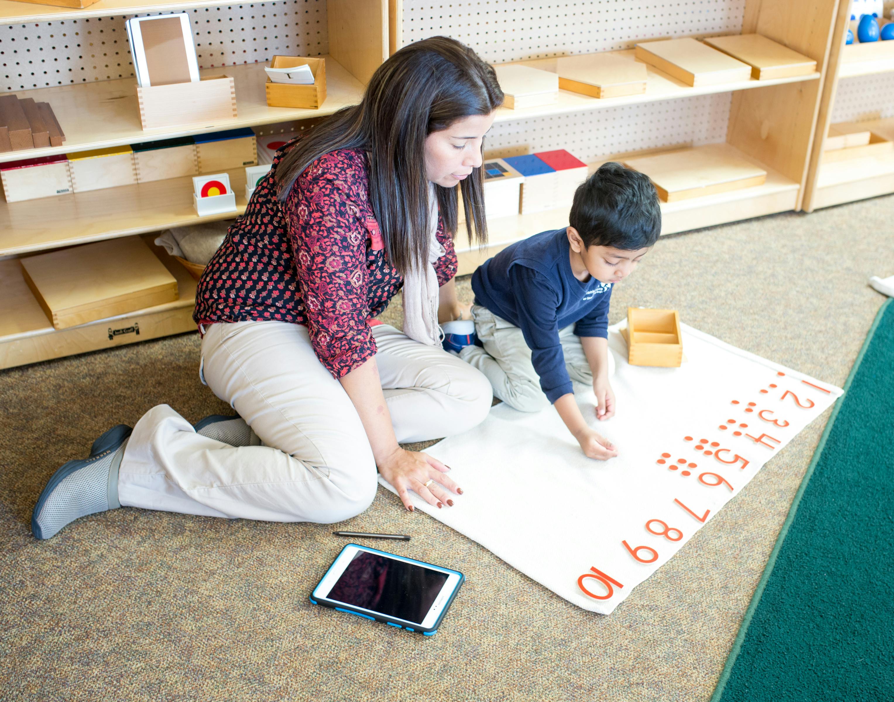 Adult and child kneeling on floor, working with numbers on a mat