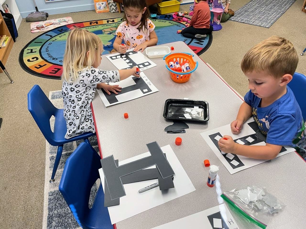 Three children at a table doing an activity with paper and small objects