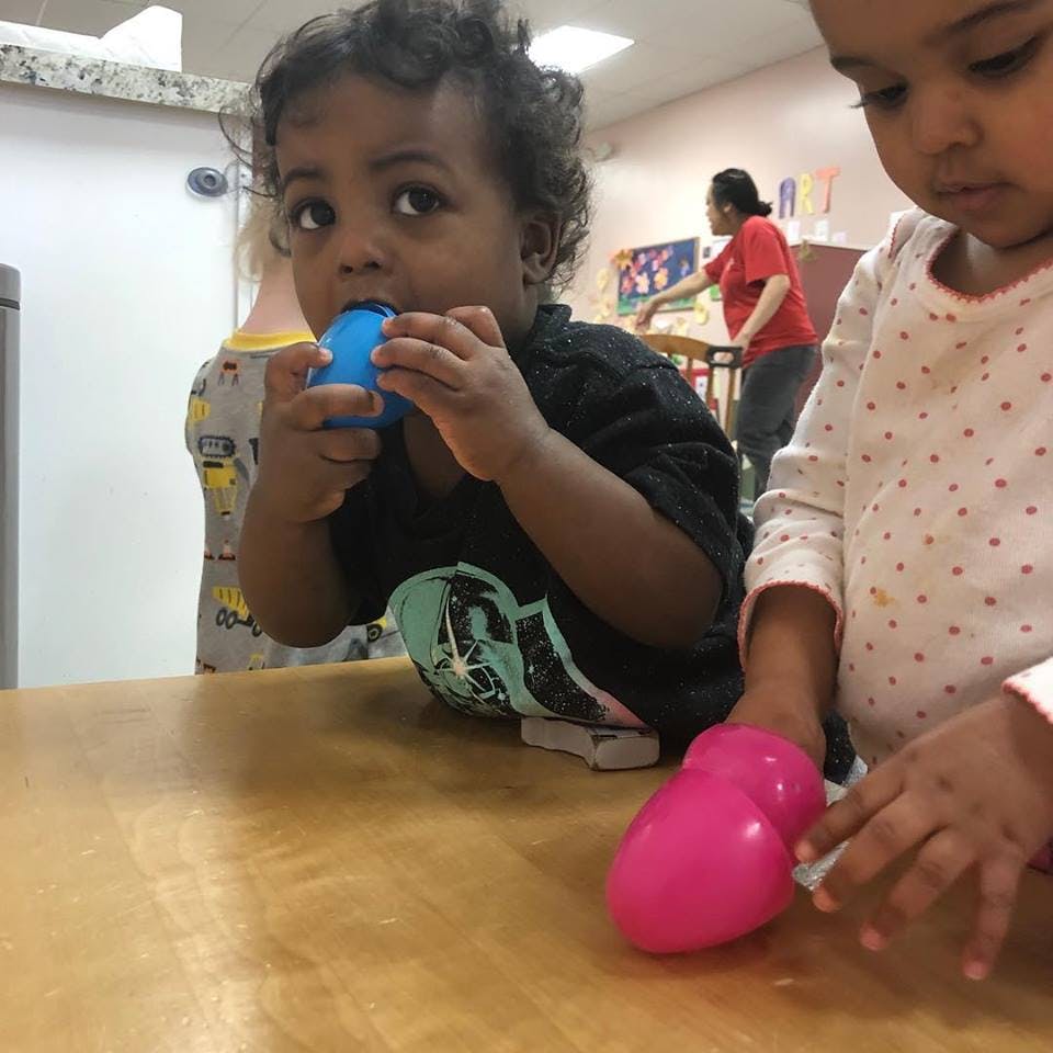 Child holding a blue object to their mouth, another child with a pink object