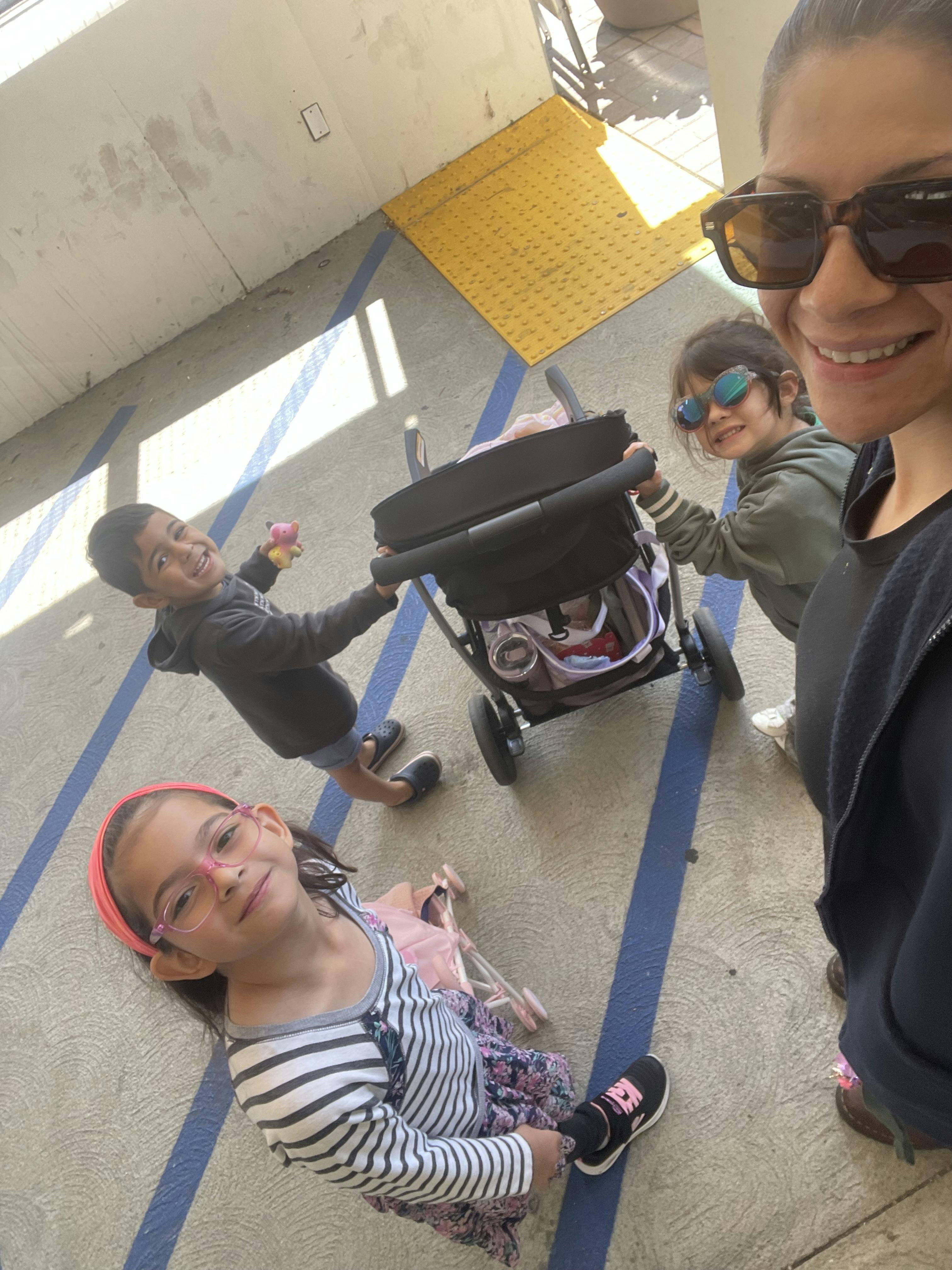Person in sunglasses taking a selfie with two children pushing a stroller