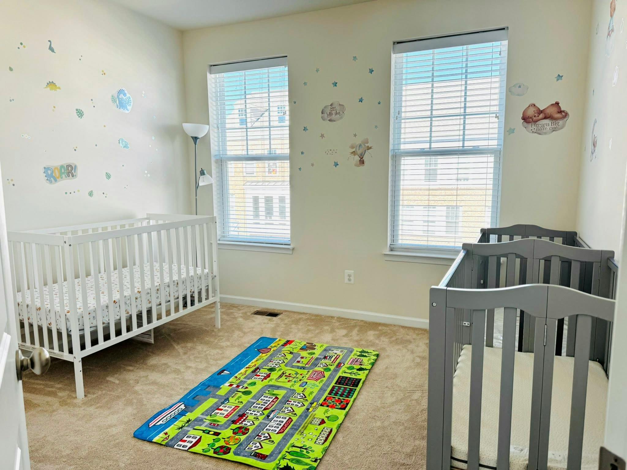 A nursery room with two cribs, wall decals, and a playmat