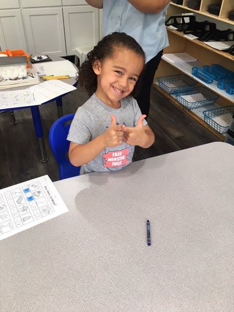 Child sitting at a desk giving two thumbs up