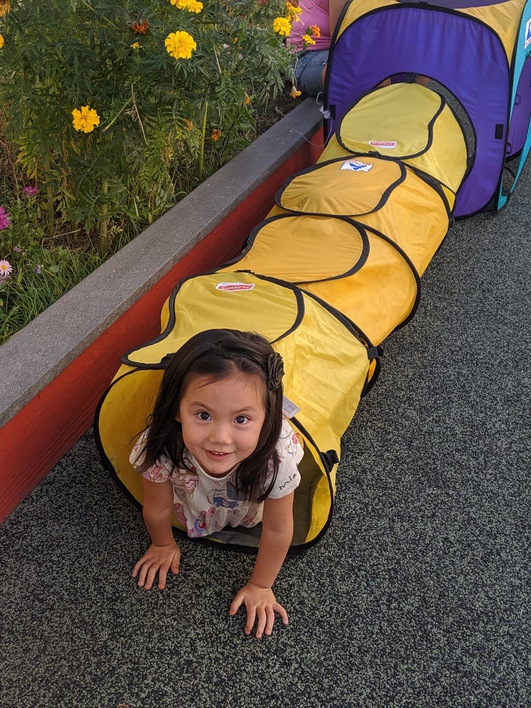 Child crawling out of a yellow play tunnel